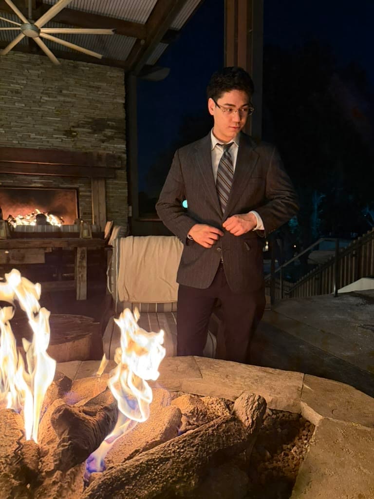 Braxton Mondell in a pinstripe suit beside a fire pit at night