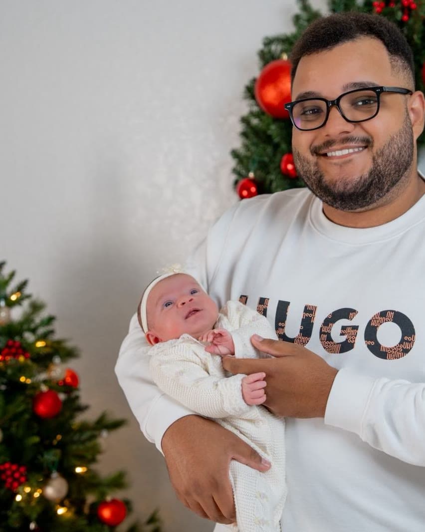 Cayo Lima smiling and holding his newborn in front of Christmas decorations